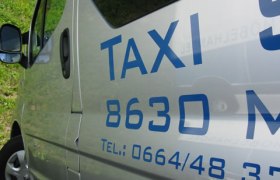 Taxi Scheucher, © Taxi Scheucher Nahaufnahme eines silbernen Taxis mit blauer Aufschrift und Telefonnummer.
