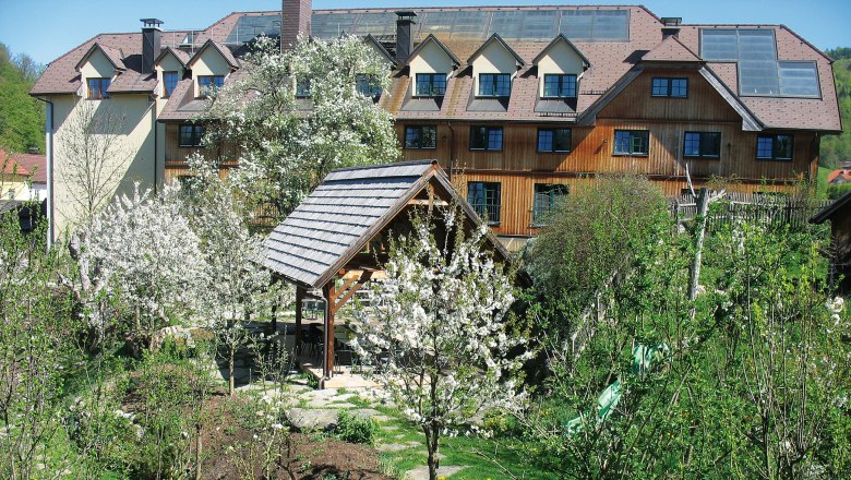 Hotel im idyllischen Dirndltal, © Steinschalerhof Naturhotel Ein Hotel im Dirndltal mit blühenden Bäumen und Garten.