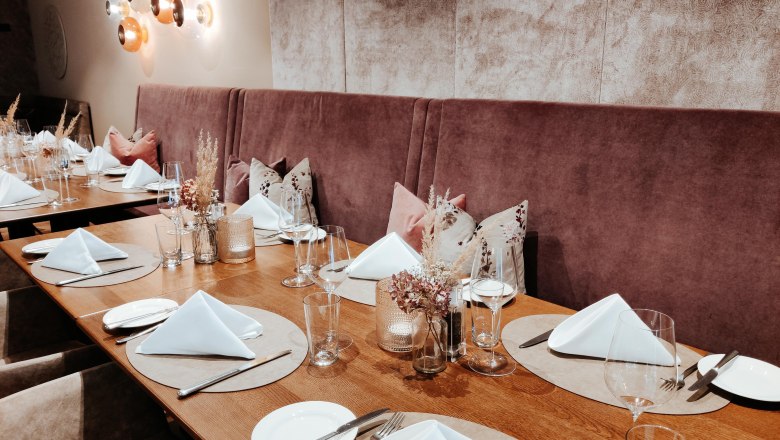 Restaurant Wintergarten Tisch gedeckt, © Hotel Schachner_miku Media Ein elegant gedeckter Tisch in einem Restaurant mit weißen Servietten, Gläsern und Besteck auf Holzoberfläche.