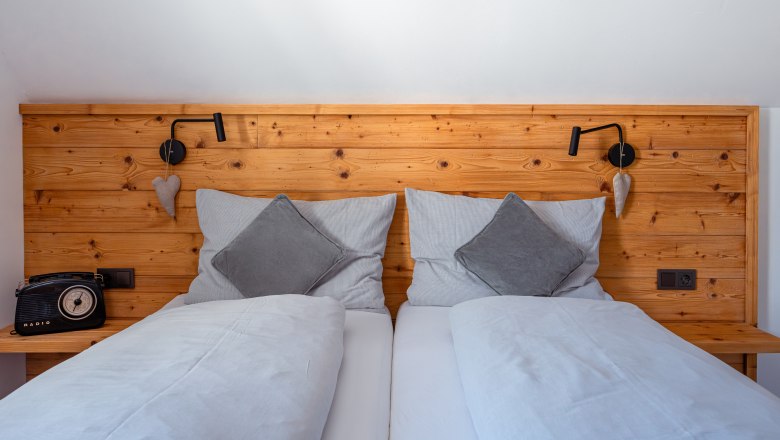 Leopold an der Ybbs, © © Niederösterreich Werbung/ Maximilian Pawlikowsky Gemütliches Doppelbett mit Holzrückwand, grauen Kissen und Decken. Links ein Retro-Radio, rechts eine Leselampe und Herzdeko.