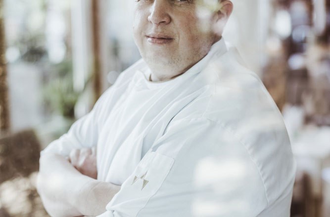 Wirt Christian Widgruber, © Niederösterreich Werbung/David Schreiber Ein Mann in Kochkleidung steht mit verschränkten Armen hinter einer Glasscheibe.