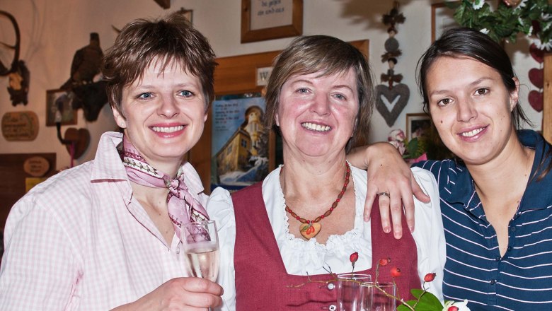 Mitzi und ihre Töchter, © Holzhof Drei Frauen lächeln in die Kamera und halten Sektgläser in der Hand.
