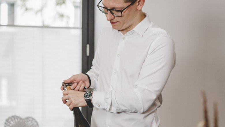 Andreas Graf leitet mit Zeitgeist und Weitblick das familiäre Restaurant, © Niederösterreich-Werbung/David Schreiber Ein Mann öffnet eine Weinflasche an einem gedeckten Tisch mit Essen.