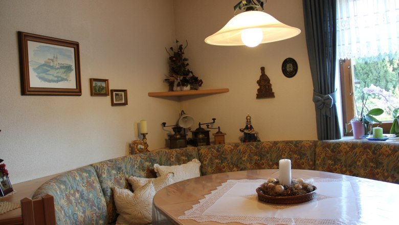 Frühstücksraum, © Haus Regina Gemütlicher Frühstücksraum mit Eckbank, Tisch, Kerze und Dekorationen an der Wand.