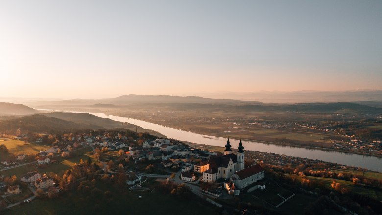 Wallfahrtsort Maria Taferl, © Niederösterreich Werbung/thecreatingclick.com Luftaufnahme einer Kirche bei Sonnenuntergang, umgeben von Fluss und Landschaft.