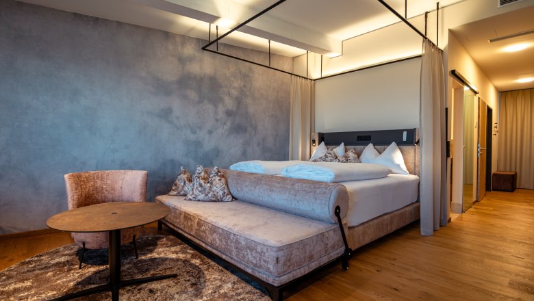 Hotel Schachner, © Niederösterreich Werbung / Maximilian Pawlikowsky Modernes Hotelzimmer mit Himmelbett, Sessel und Tisch auf Holzboden.