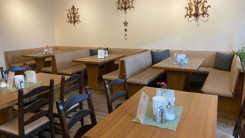 Frühstücksbereich, © Wiener Alpen Gemütlicher Frühstücksbereich mit Holztischen und gepolsterten Sitzbänken, dekoriert mit Wandornamenten.