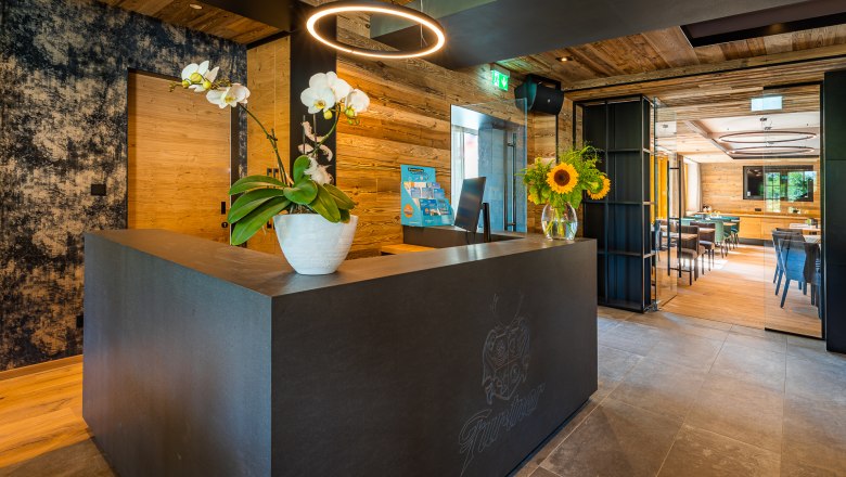 Rezeption, © Christian Kremsl Moderne Rezeption mit Holzverkleidung, Orchideen und Sonnenblumen auf dem Tresen.