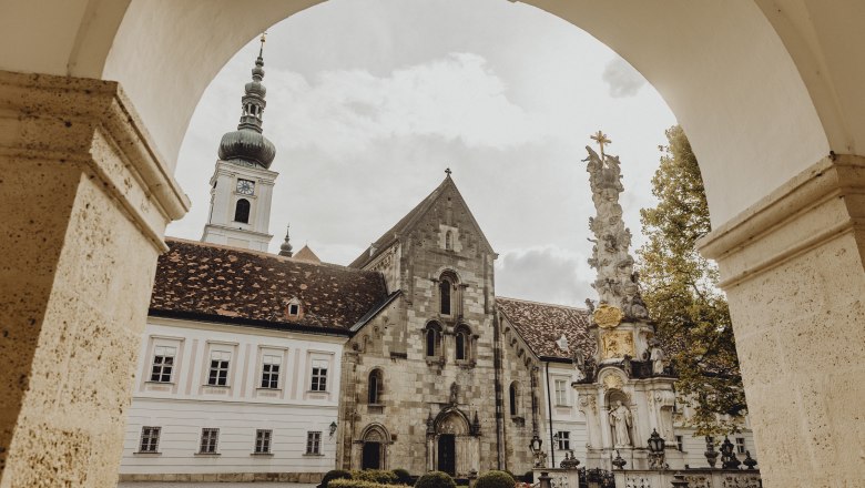 Gasthof, Stift und Klosterladen, © Niederösterreich Werbung/Sophie Menegaldo Blick durch einen Torbogen auf ein historisches Klostergebäude mit Turm und einer barocken Säule im Vordergrund.