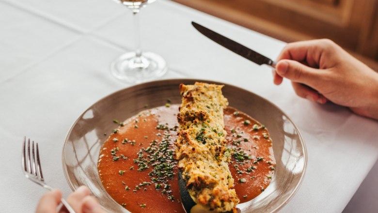Gefüllte Zucchini mit Tomatensauce, © Niederösterreich Werbung/Daniela Führer Gefüllte Zucchini mit Tomatensauce auf einem Teller, daneben ein Glas Weißwein.