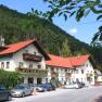 Gasthof, © Gasthof zur Bruthenne Ein traditioneller Gasthof mit roten Dächern und Blumenkästen, umgeben von Wald und geparkten Autos.
