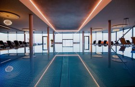 Infinitypool innen, © Hotel Schachner_MIKU Media Innenansicht eines Infinitypools mit Liegestühlen und großen Fenstern.