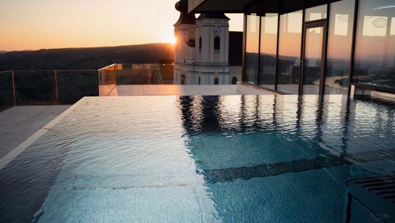 Infinitypool Abendstimmung Hotel Schachner, © Hotel Schachner_MIKU Media Infinitypool bei Sonnenuntergang mit Blick auf ein Gebäude und die Landschaft.