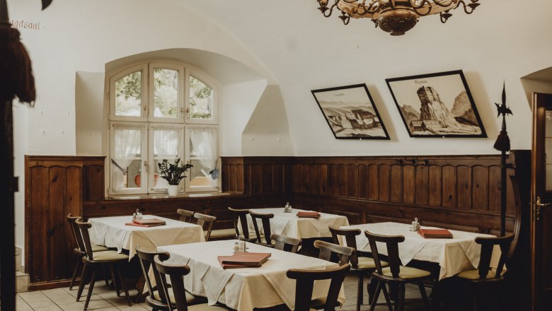 Gemütlicher Gastraum mit Holzmöbeln, weißen Tischdecken und Wandbildern.