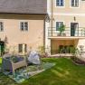 Garten mit Sitzgelegenheit vor einem alten Gebäude mit gelber Fassade und grünen Fensterrahmen.
