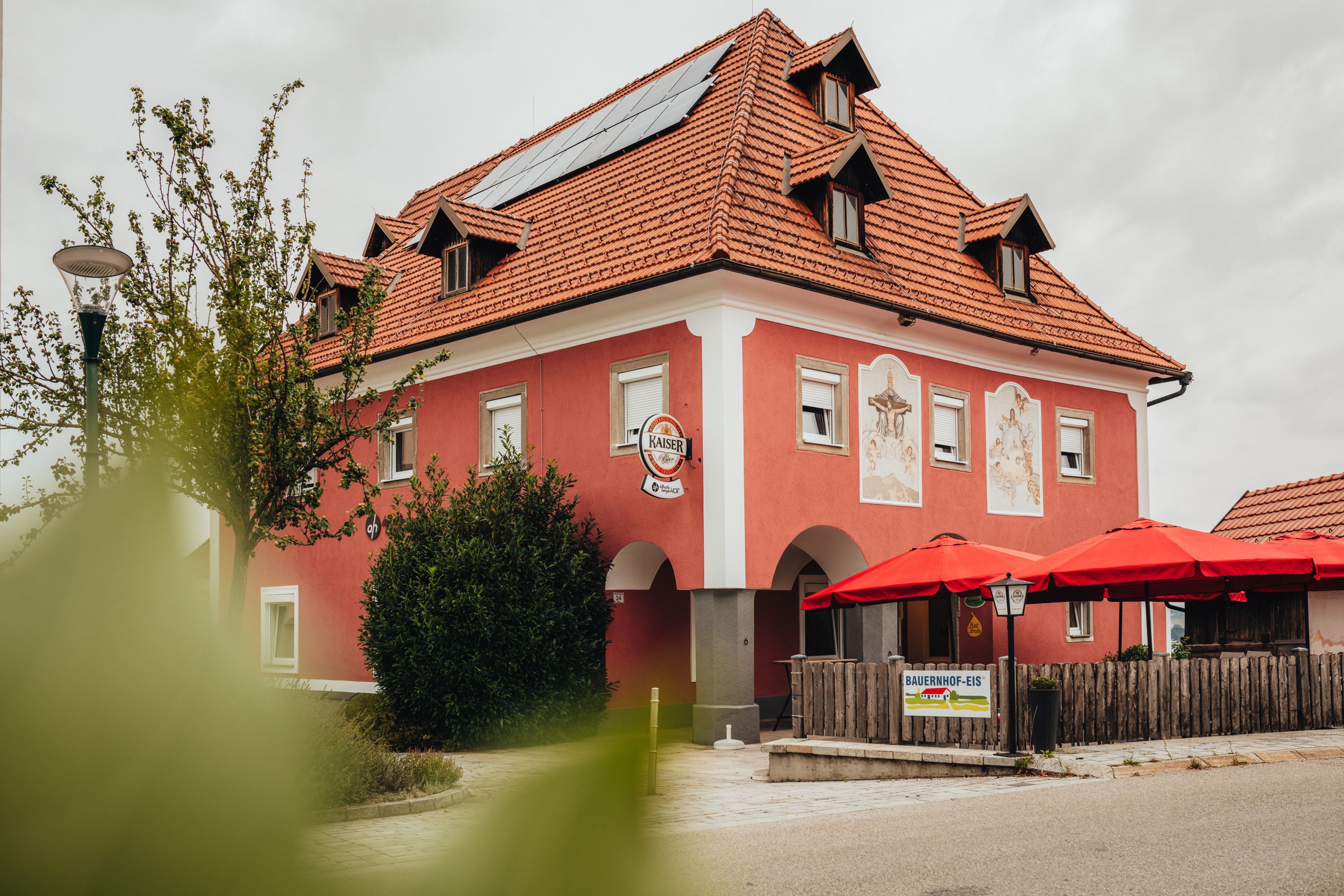 Ein rotes Gebäude mit roten Sonnenschirmen und Solarpanelen auf dem Dach.