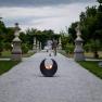 Ein Kiesweg im historischen Hofgarten des Stifts Seitenstetten mit Skulpturen und Pflanzen, im Vordergrund eine Feuerstelle.