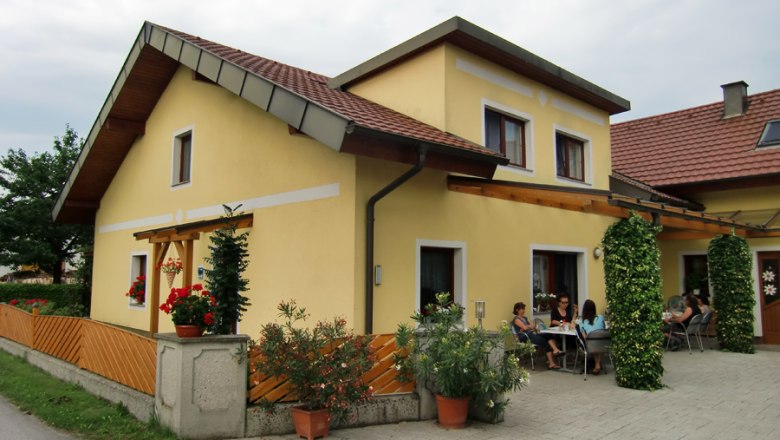 Gelbes Haus mit Terrasse und Menschen, die drau&szlig;en sitzen.
