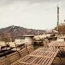 Leere Terrasse mit Holztischen und -st&uuml;hlen, Berglandschaft im Hintergrund.