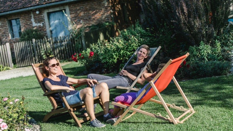 Drei Personen entspannen auf Liegestühlen im Garten.