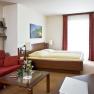Gemütliches Hotelzimmer mit Doppelbett, rotem Sofa, Glastisch und Dekorationen.