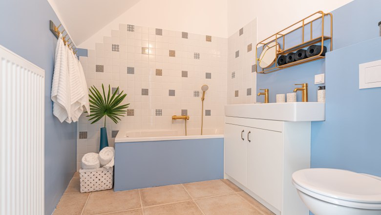 Modernes Badezimmer mit blauen W&auml;nden, Badewanne, Waschbecken und goldenen Armaturen.