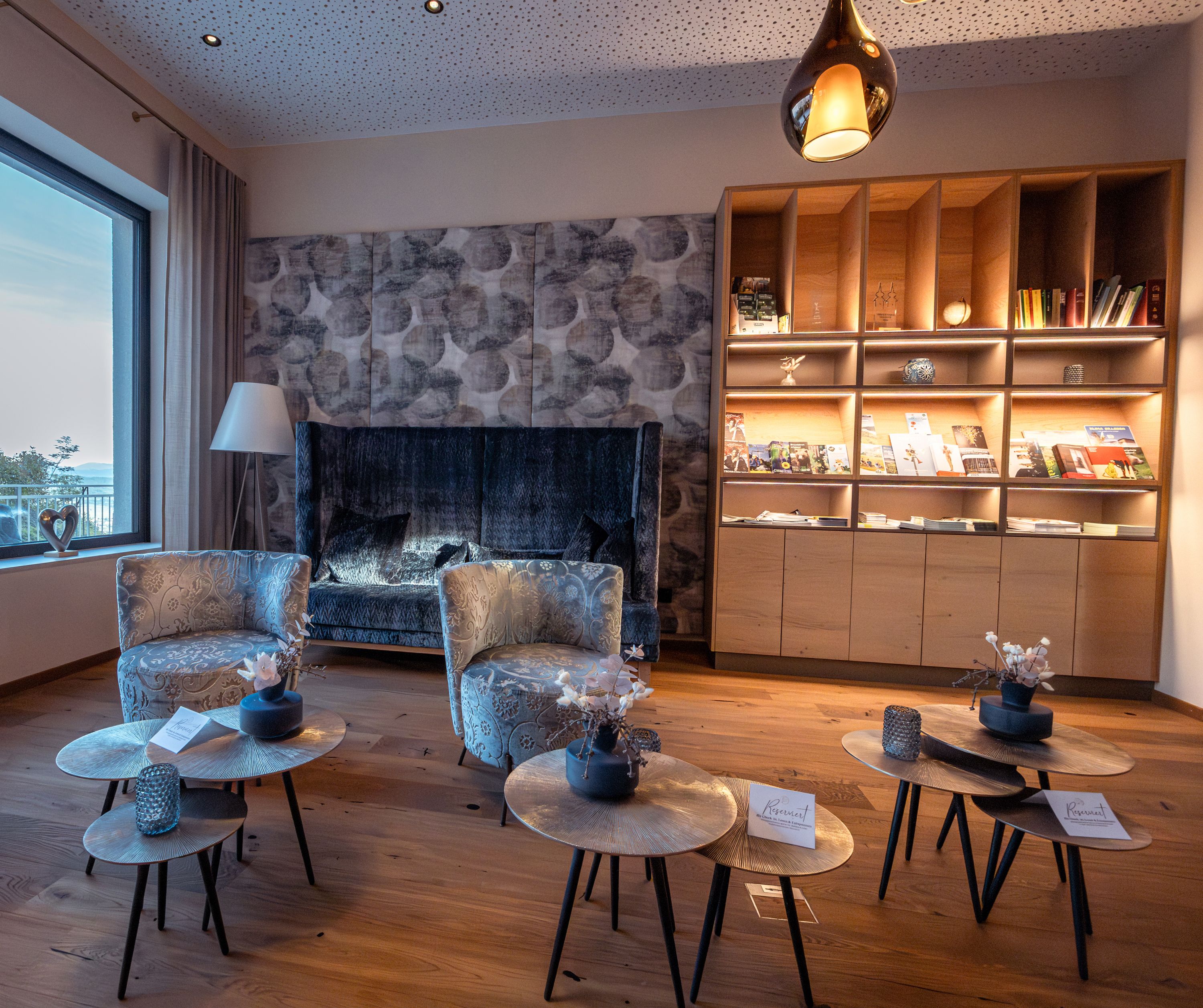 Gemütlicher Hotel-Loungebereich mit Sesseln, Couchtischen und Bücherregal.