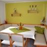 Gem&uuml;tliche Sitzecke mit Eckbank und Tisch in einem Fr&uuml;hst&uuml;cksraum, dekoriert mit gr&uuml;nen Akzenten und Blumen.