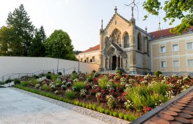 Eine Kirche mit gotischen Elementen und einem gepflegten Garten voller Blumen im Vordergrund.