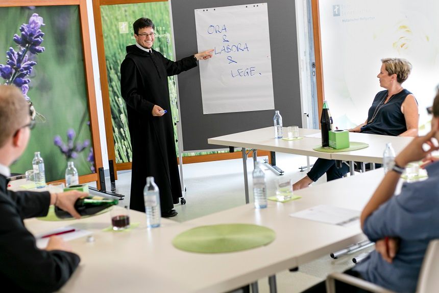 Ein Seminar im Stift Seitenstetten mit einem Vortragenden in Mönchskleidung, der auf ein Flipchart zeigt. Teilnehmer sitzen an Tischen.