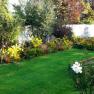 Ein gepflegter Garten mit grüner Wiese, bunten Blumenbeeten und einer weißen Mauer im Hintergrund.