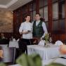 Eine Chefköchin und ein Mann in traditioneller Kleidung stehen lächelnd in einem eleganten Restaurant.