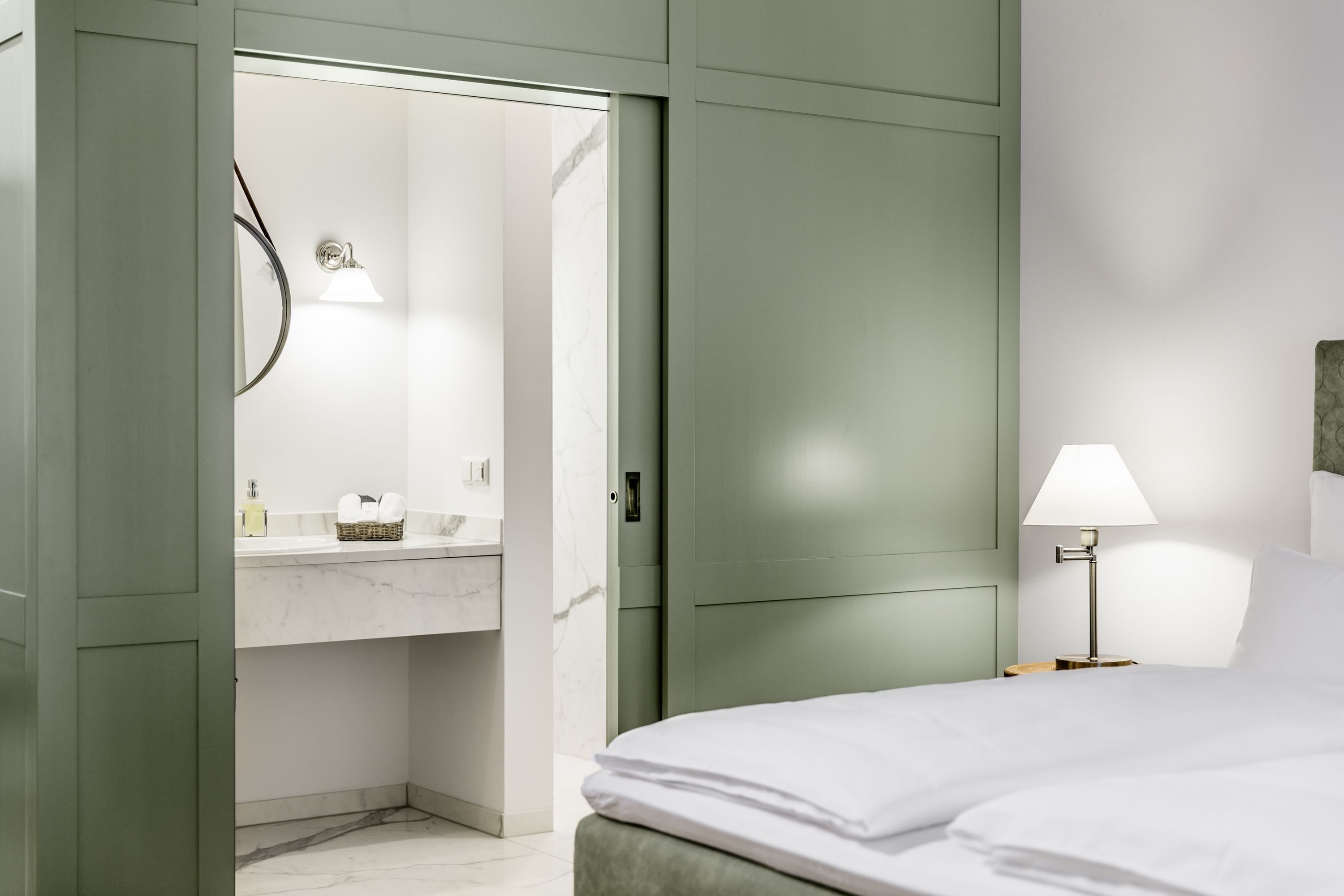 Hotelzimmer mit grünem Schiebetürenschrank, Bett und Blick ins Badezimmer.