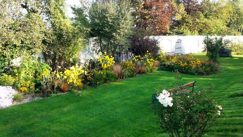 Ein gepflegter Garten mit grüner Wiese, bunten Blumenbeeten und einer weißen Mauer im Hintergrund.