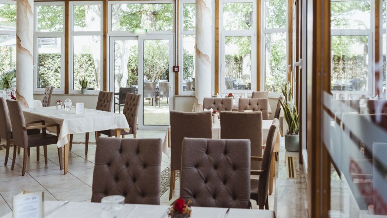 Innenansicht eines eleganten Restaurants mit gedeckten Tischen und gro&szlig;en Fenstern.