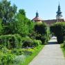 Ein gepflegter Gartenweg mit Blumen und Bäumen, im Hintergrund ein historisches Gebäude mit Türmen.