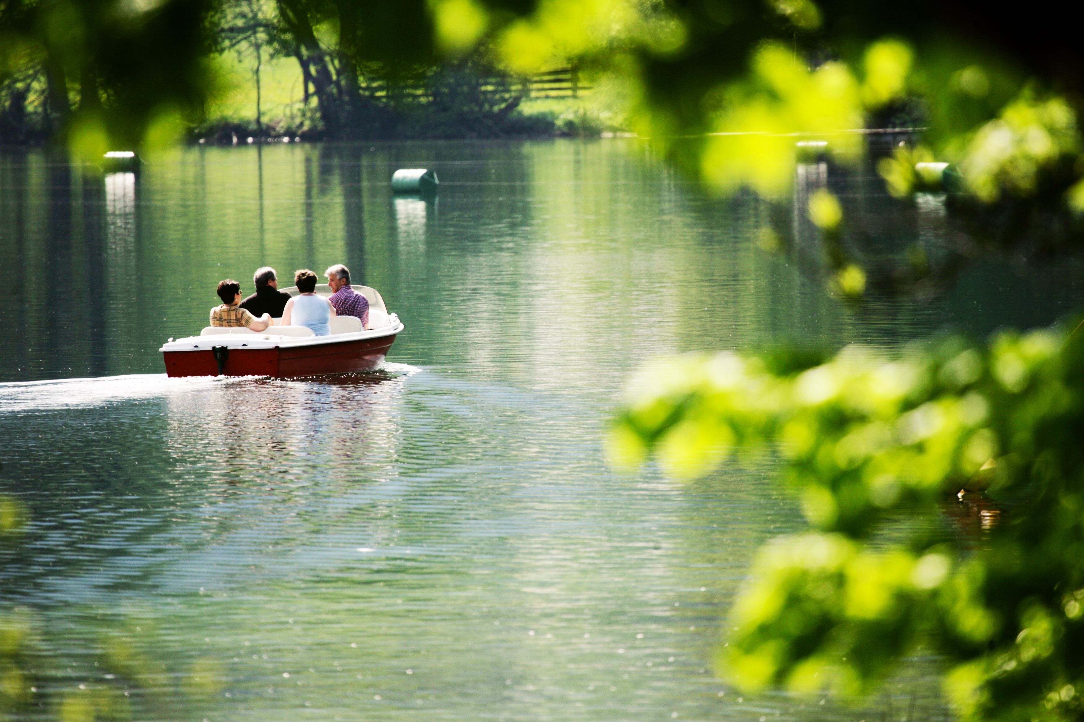 Vier Personen in einem Boot auf einem ruhigen See, umgeben von grüner Natur.