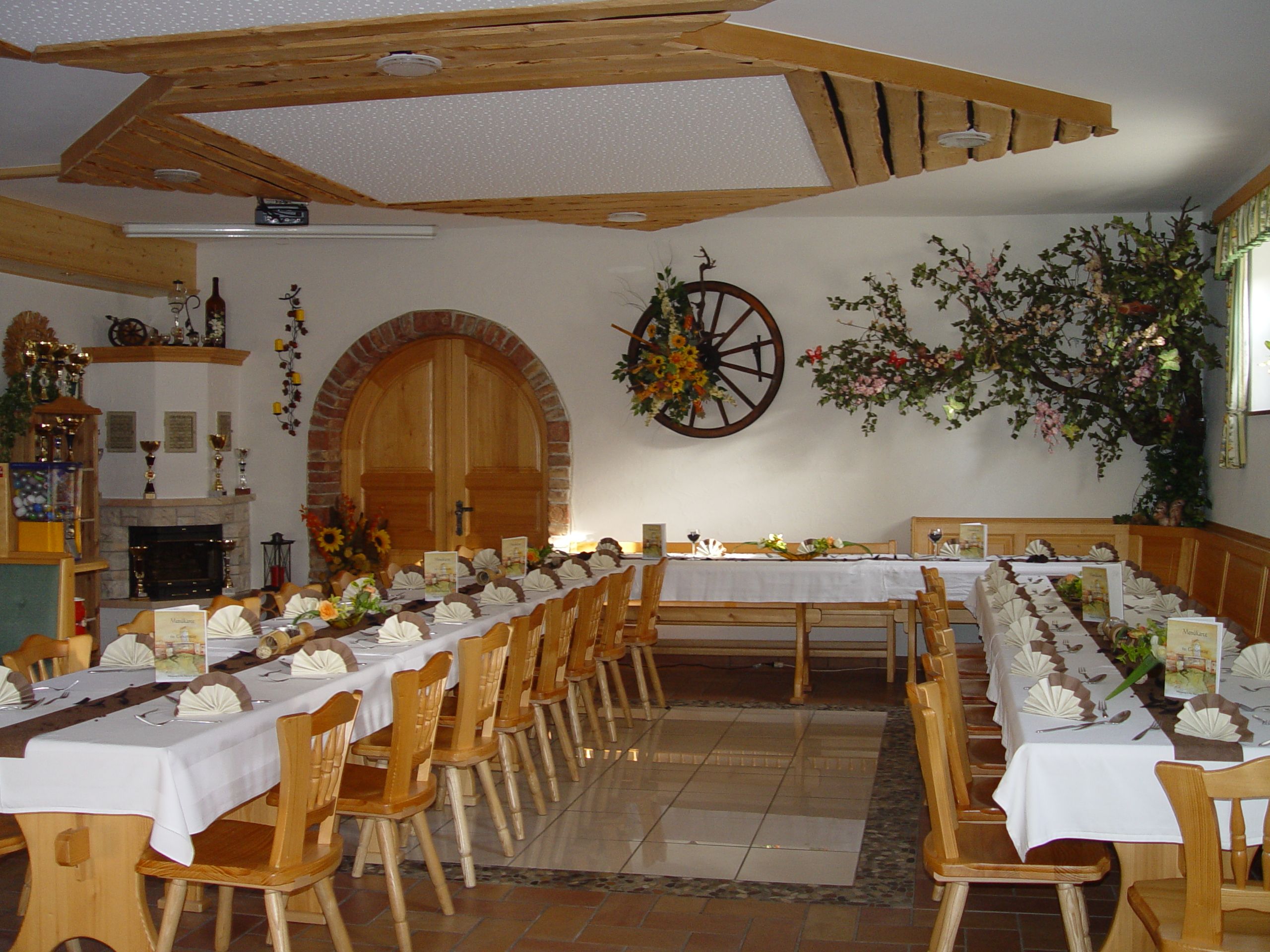 Ein festlich gedeckter Gastraum mit langen Tischen, dekoriert mit Blumen und Servietten, in einem rustikalen Ambiente.