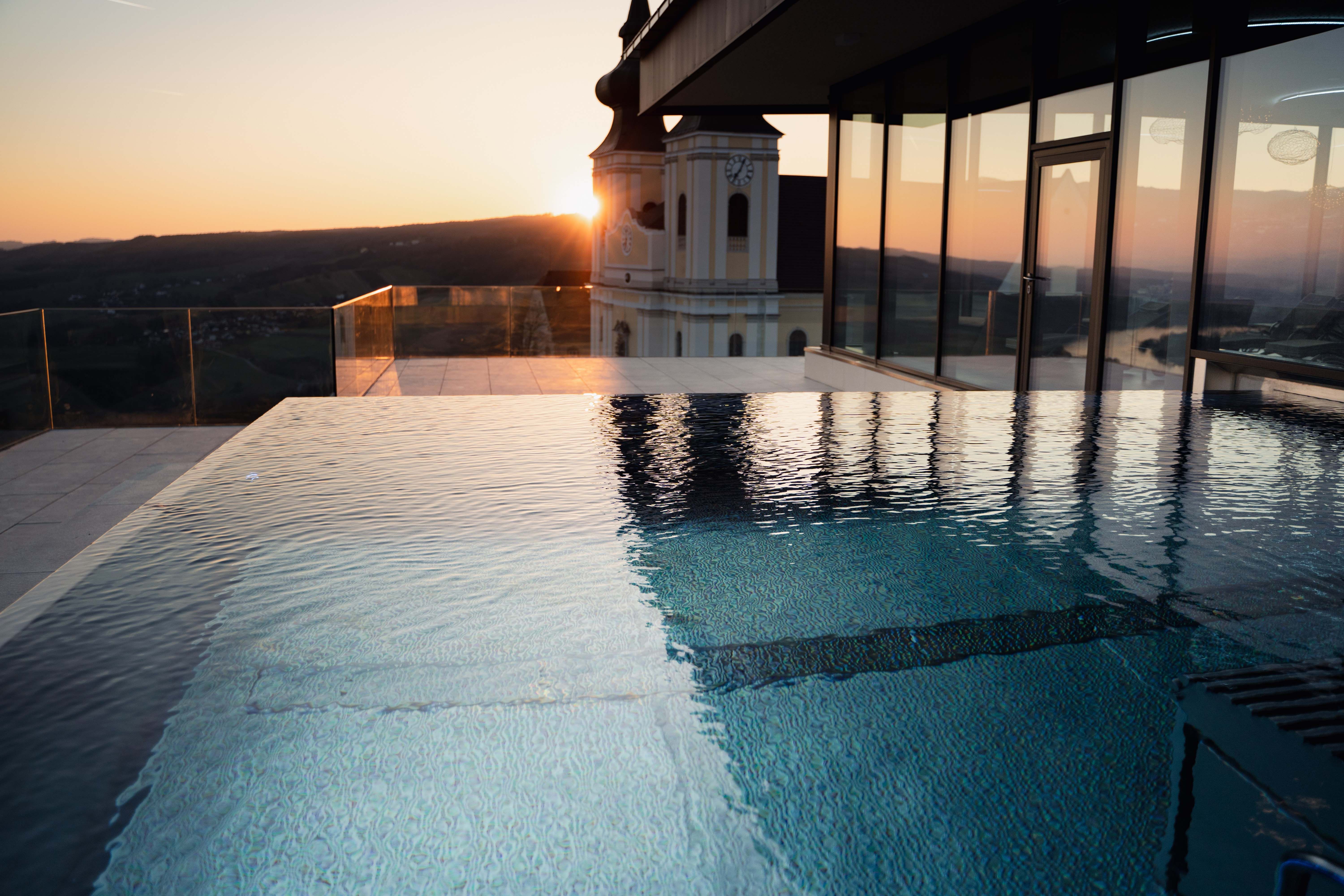 Infinitypool bei Sonnenuntergang mit Blick auf ein Gebäude und die Landschaft.