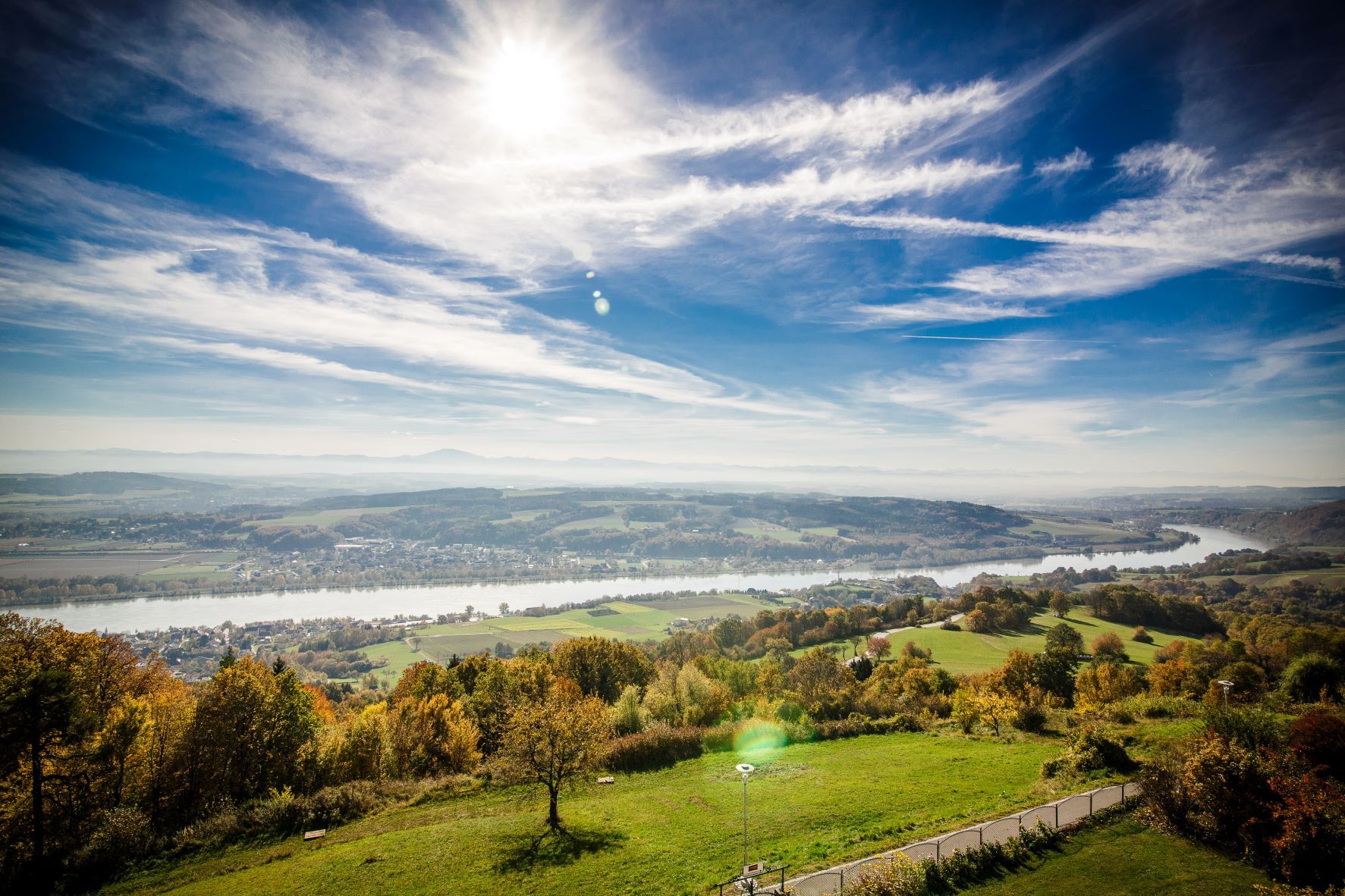 Panoramablick auf eine Flusslandschaft mit grünen Feldern und blauem Himmel.