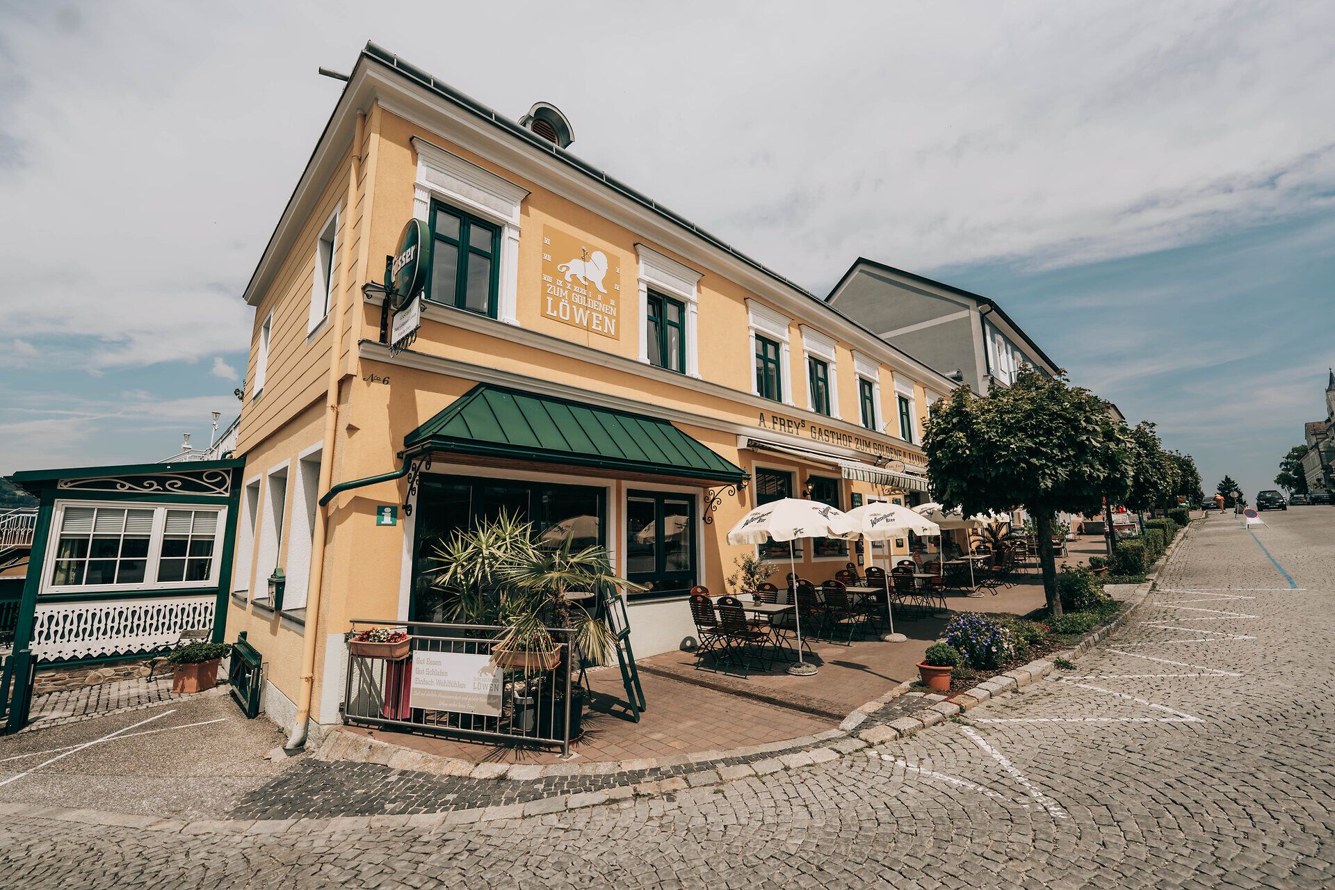 Außenansicht eines gelben Gasthauses mit Terrasse und Sonnenschirmen.