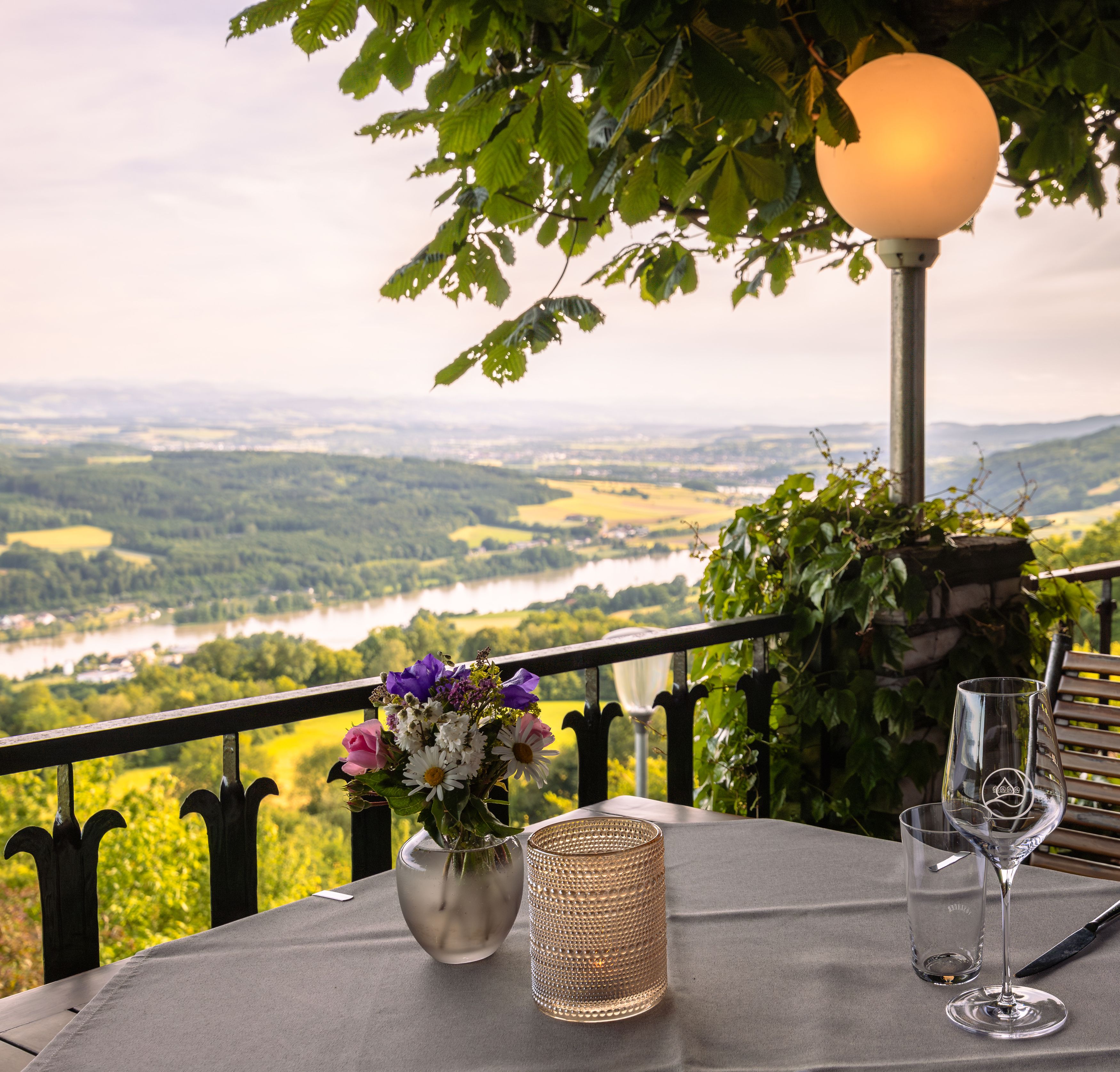 Terrasse mit Tisch, Blumen und Blick auf Flusslandschaft.