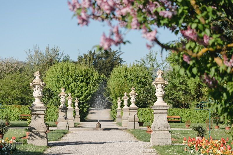 Ein gepflegter Gartenweg mit Statuen und blühenden Bäumen im Frühling.