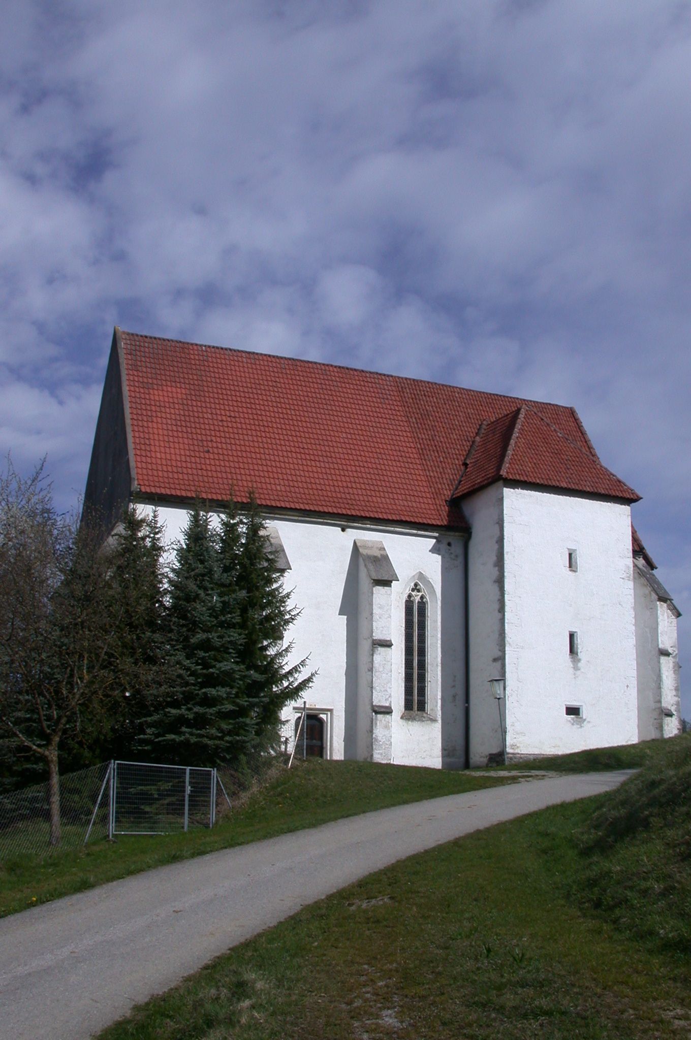 Andreaskirche in Kirchberg an der Pielach mit rotem Ziegeldach und weißer Fassade, umgeben von Bäumen und einem Weg im Vordergrund.