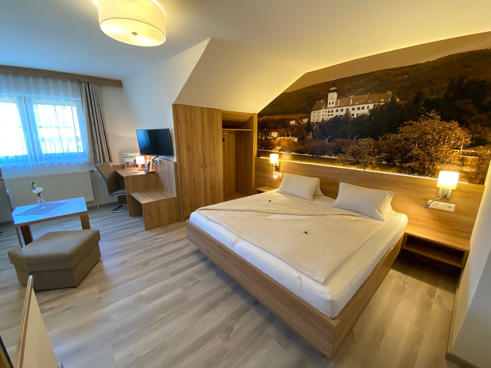 Modernes Hotelzimmer mit Doppelbett, Schreibtisch, Fernseher und großem Wandbild.
