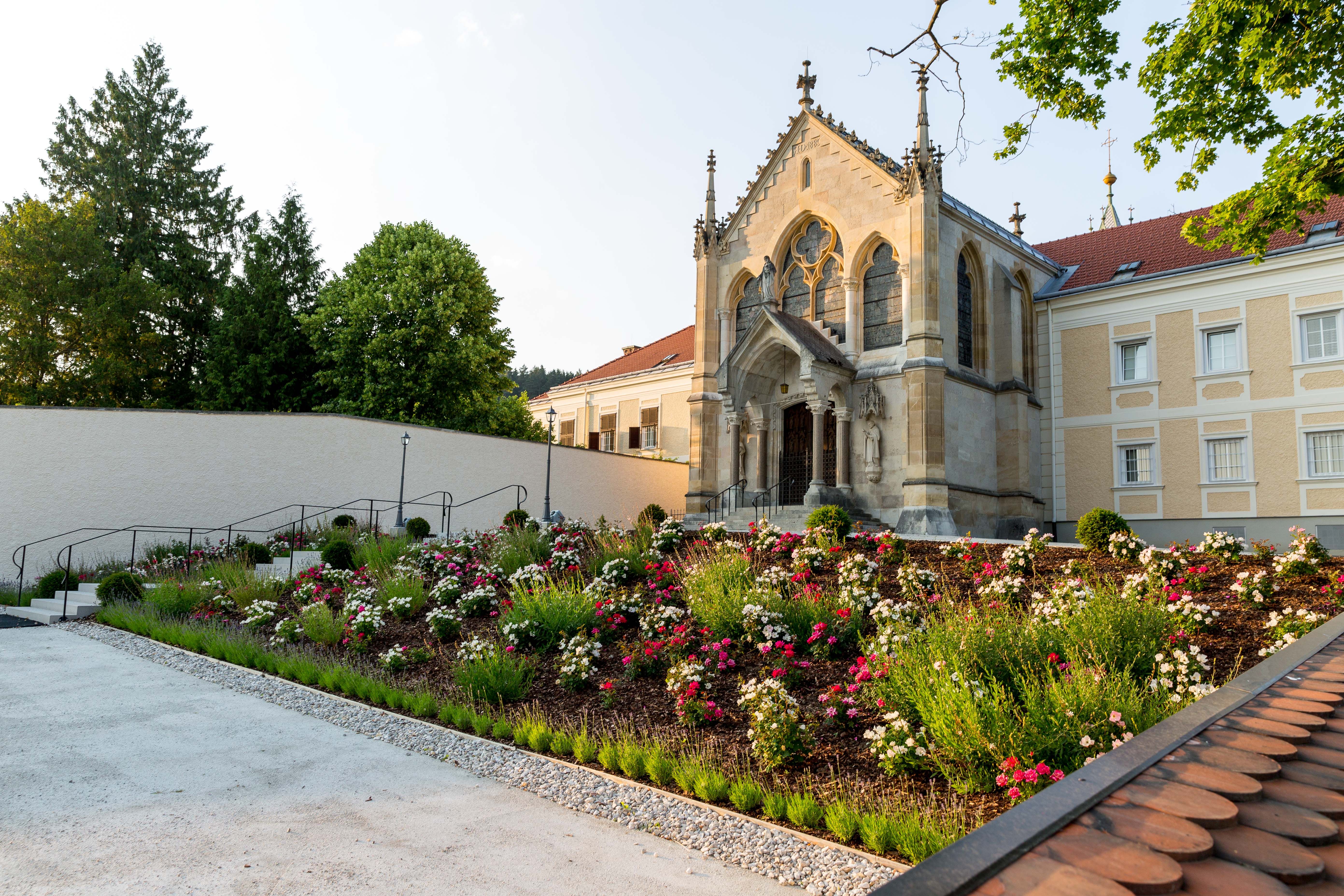 Eine Kirche mit gotischen Elementen und einem gepflegten Garten voller Blumen im Vordergrund.