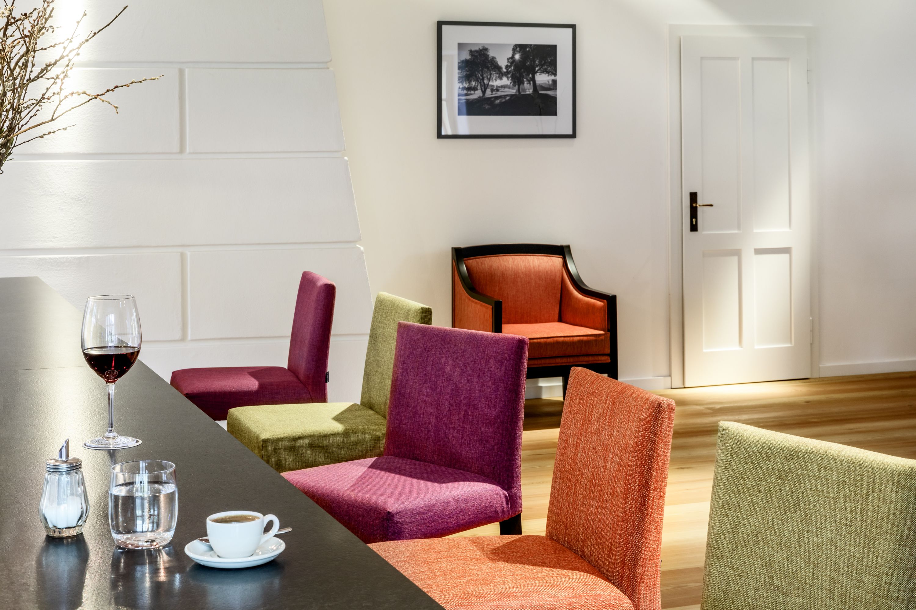 Innenansicht eines modernen Hotel-Lounges mit bunten Stühlen, einem Tisch mit Getränken und einem Bild an der Wand.