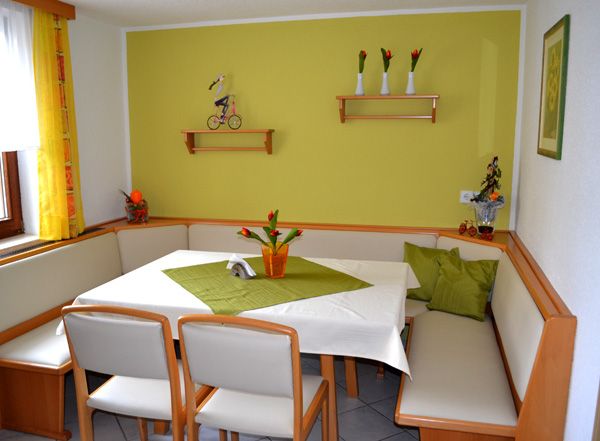 Gemütliche Sitzecke mit Eckbank und Tisch in einem Frühstücksraum, dekoriert mit grünen Akzenten und Blumen.