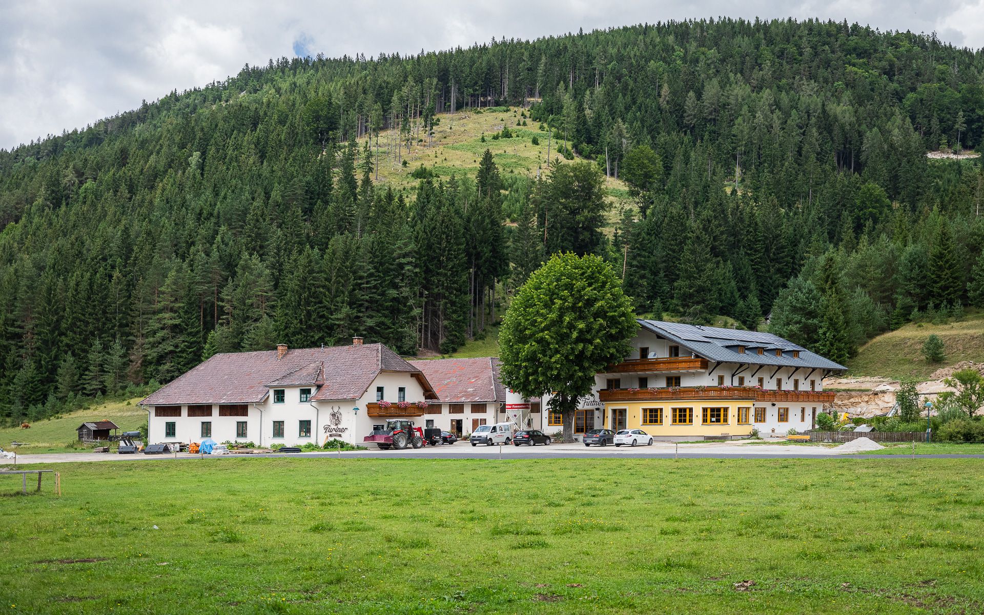 Gasthof Furtner vor bewaldetem Hügel.