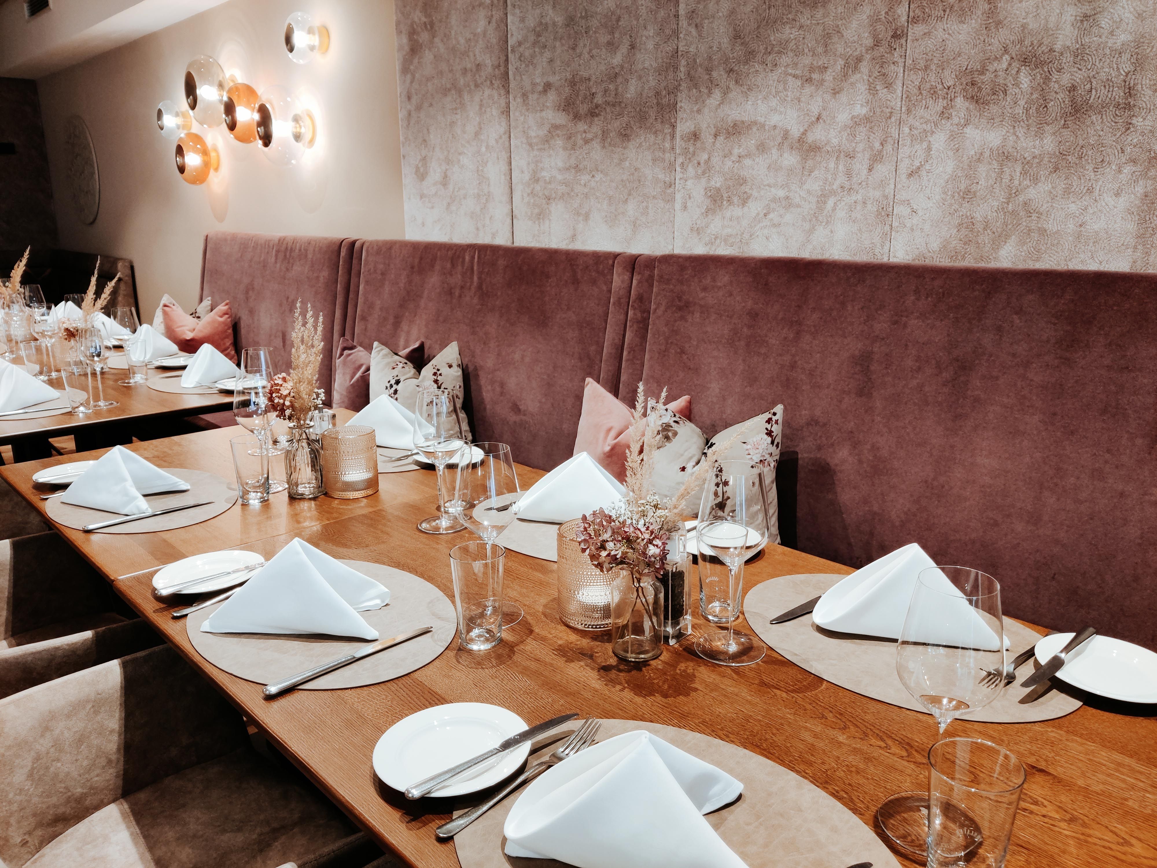Ein elegant gedeckter Tisch in einem Restaurant mit weißen Servietten, Gläsern und Besteck auf Holzoberfläche.